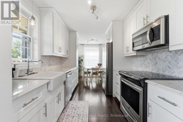 Long galley kitchen with white cabinets, stainless steel appliances, and dark hardwood floors. - 770 Scott Street W, North Perth