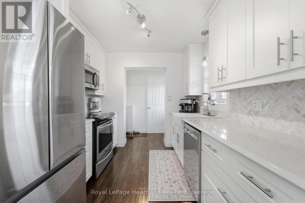 Kitchen with white cabinets, stainless steel appliances, granite countertops, and dark hardwood floors. - 770 Scott Street W, North Perth