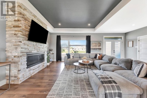 Living room with a large sectional sofa, stone fireplace with mounted television, and a window view. - 7700 Copeland Road, Ottawa