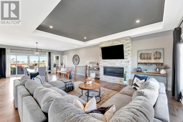 Spacious living and dining area with hardwood floors, a large sectional, stone fireplace, and patio doors. - 7700 Copeland Road, Ottawa