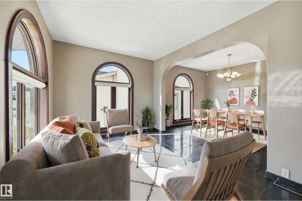 Living room with a large arched window, beige sofa, two armchairs, and a coffee table on a patterned rug. - 7708 158 Av Nw, Edmonton