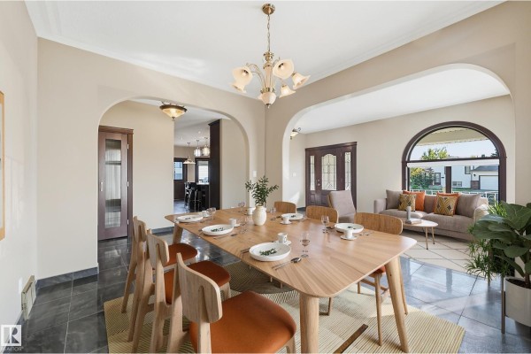 Formal dining room with a large wooden table, six chairs, and arched windows overlooking a suburban street. - 7708 158 Av Nw, Edmonton
