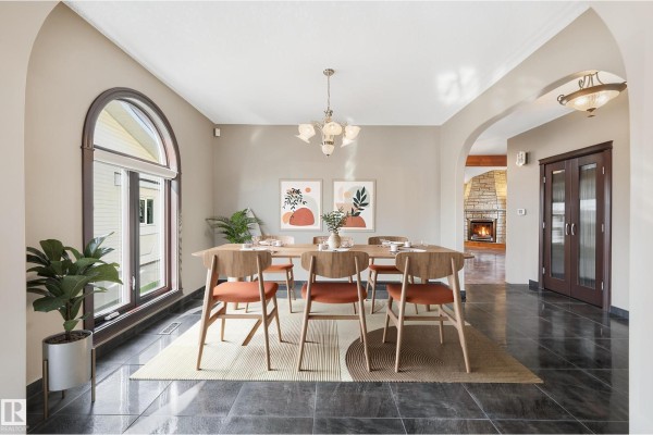 Dining room featuring a wooden table, chairs with orange cushions, arched windows, and a glimpse of a living room fireplace. - 7708 158 Av Nw, Edmonton