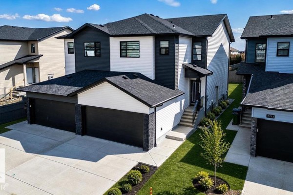 Exterior view of a duplex with a black roof, dark grey and white siding, and a triple car garage. - 7709 174a Av Nw, Edmonton
