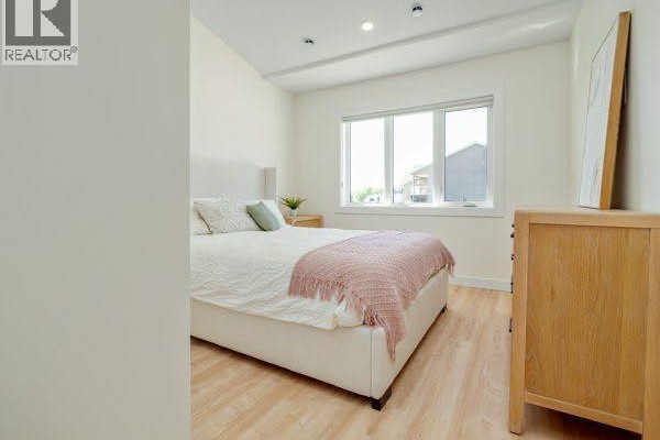 Bedroom with a queen-sized bed, pink throw blanket, wooden dresser, and a large window. - 771 7 Avenue W, Cardston