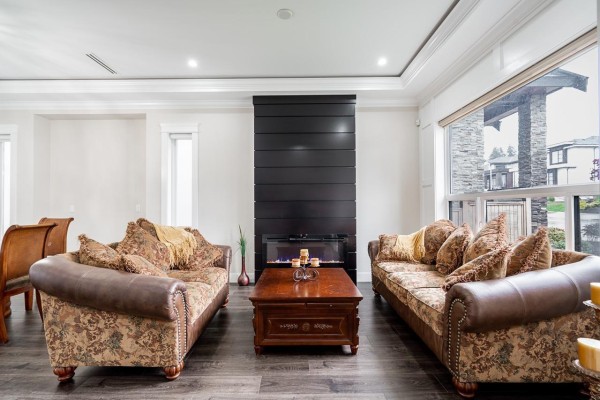 Living room with two patterned sofas, a dark wood coffee table, and a modern black fireplace. - 7719 155 Street, Surrey