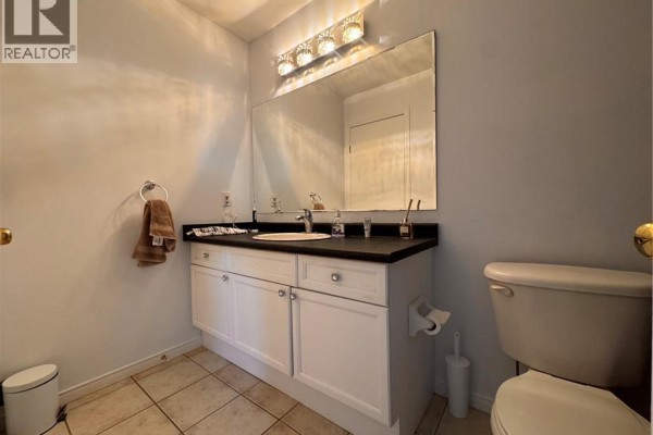 A bathroom vanity with a white countertop, white cabinets, a stainless steel sink, and a large mirror above. - 772 Zermatt Drive, Waterloo