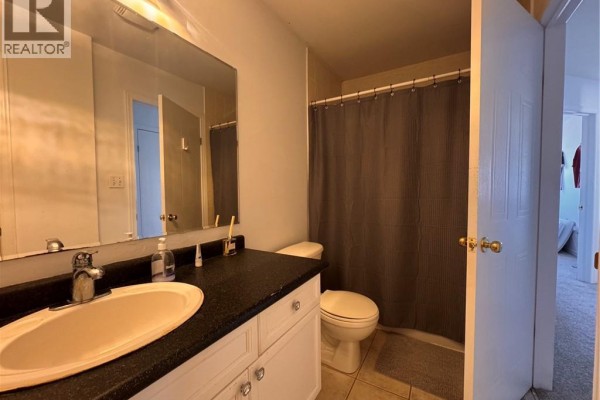 A bathroom with a vanity, toilet, and a dark gray shower curtain against a tiled floor and light gray walls. - 772 Zermatt Drive, Waterloo