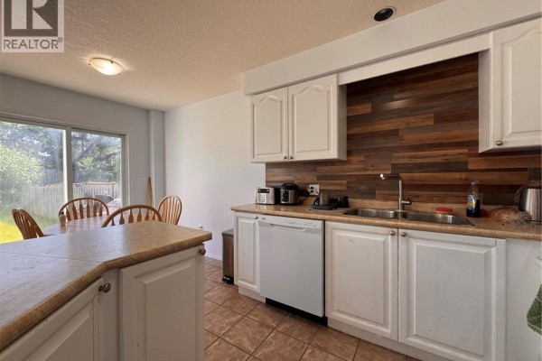 A kitchen with white cabinets, a double sink, dishwasher, and a dining table with wooden chairs next to a sliding glass door. - 772 Zermatt Drive, Waterloo