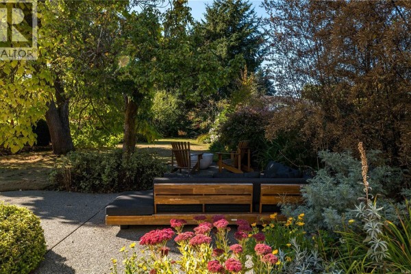 Backyard patio with wooden outdoor sofa and chairs surrounded by lush greenery. - 773 Middleton St, Saanich