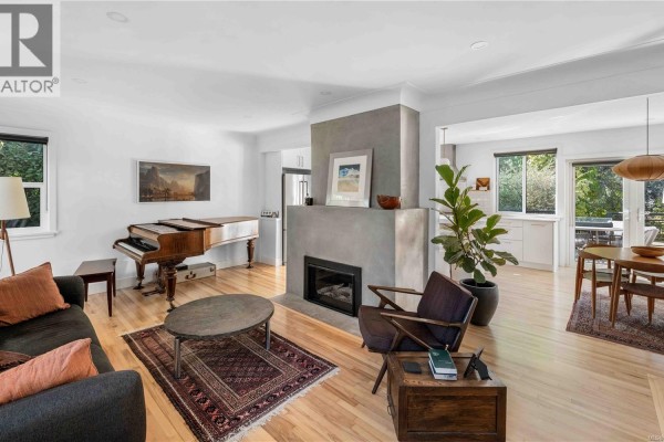 Living room with hardwood floors, grey fireplace, piano, and modern furniture. - 773 Middleton St, Saanich