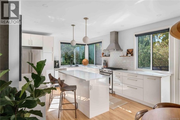 Open concept kitchen with white island, modern cabinets, stainless steel appliances, and a garden view. - 773 Middleton St, Saanich