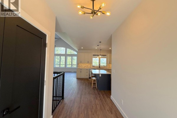 Hallway entrance with a black door, wood flooring, and a view into the living area and kitchen. - 7735 Gn Road, Grand Forks