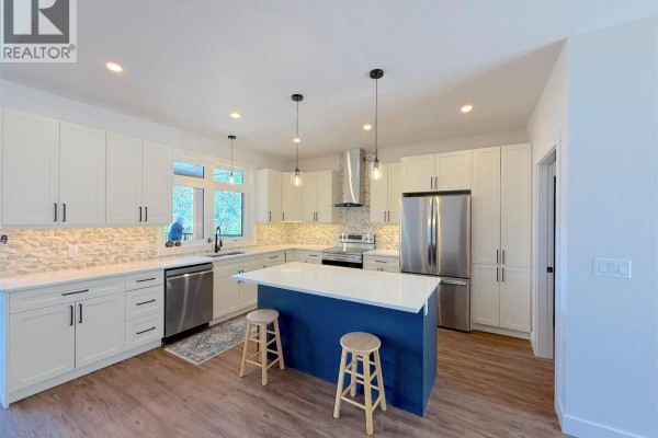 Modern kitchen with white cabinetry, a blue island with stools, stainless steel appliances, and stone backsplash. - 7735 Gn Road, Grand Forks