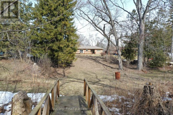 Wooden bridge over a small stream leading towards a detached house on a hill. - 774 Sutherland Avenue, Newmarket