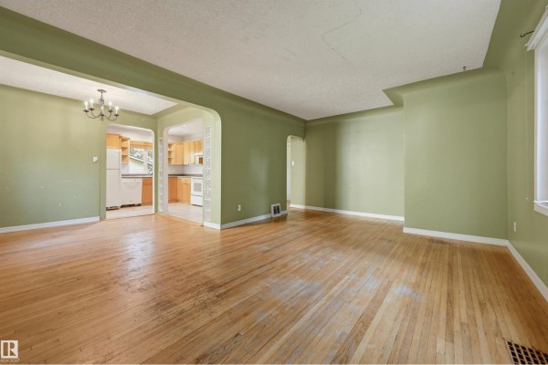 Living room and kitchen area with light green walls, hardwood floors, and an arched doorway. - 7754 80 Av Nw Nw, Edmonton