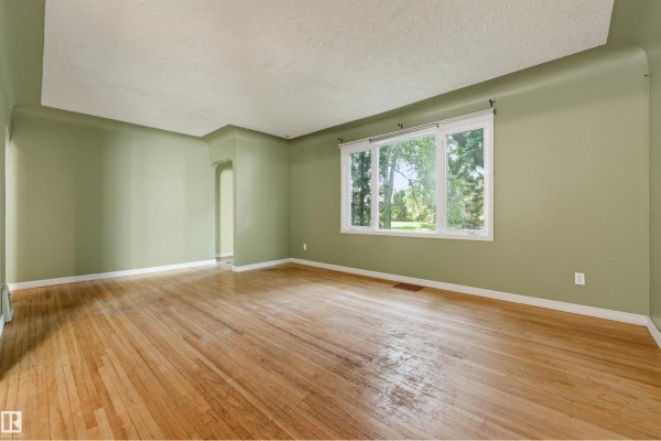 Living room with light green walls, hardwood floors, and a large window with a view of greenery. - 7754 80 Av Nw Nw, Edmonton