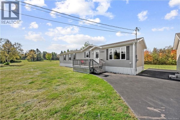Front angled view of the grey mobile home with a deck, asphalt driveway, and detached garage. - 7754 Route 134, Sainte Anne De Kent
