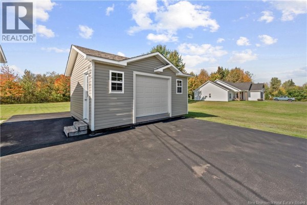 Exterior of a grey detached garage with a white garage door and two windows, beside an asphalt driveway. - 7754 Route 134, Sainte Anne De Kent