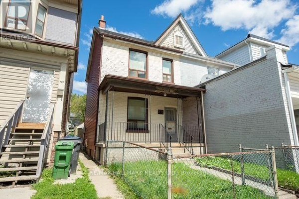 Front exterior view of a two-story brick house with a covered porch and fence. - 776 Gerrard Street E, Toronto