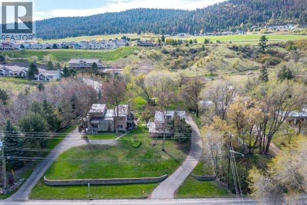 Aerial view of the property showing two houses, driveways, and landscaped grounds with hills in the background. - 7778 Okanagan Landing Road, Vernon