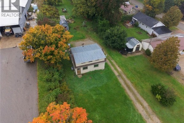 Overhead view of the beige house on a grassy lot with colorful autumn trees and a commercial building. - 77937 London Road, Clinton