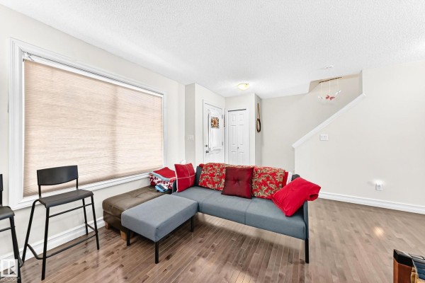 Living room with sectional sofa, ottomans, large window, and stairs to upper level. - #78 655 Tamarack Rd Nw, Edmonton