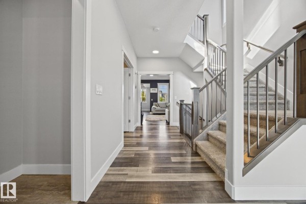 Interior hallway with a staircase on the right, hardwood floors, and doorways to rooms. - 78 Ainsley Wy, Sherwood Park