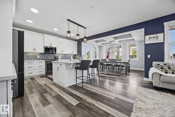 Open concept kitchen and dining area with white cabinets, a large island, dark blue accent walls, and a coffered ceiling. - 78 Ainsley Wy, Sherwood Park