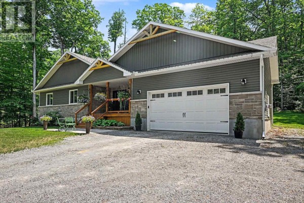 Right side of the modern house showing the white double garage door, gray siding, stone foundation, and gravel driveway. - 78 Deerfield Drive, Mcnab/braeside
