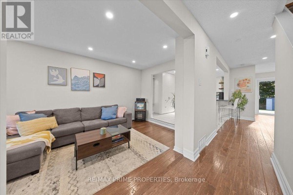 Living room with a gray sectional sofa, patterned rug, coffee table, and hardwood floors. - 78 Fieldgate Drive, Ottawa