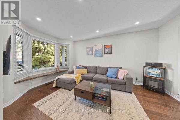 Living room with a bay window, sectional sofa, coffee table, and hardwood floors. - 78 Fieldgate Drive, Ottawa