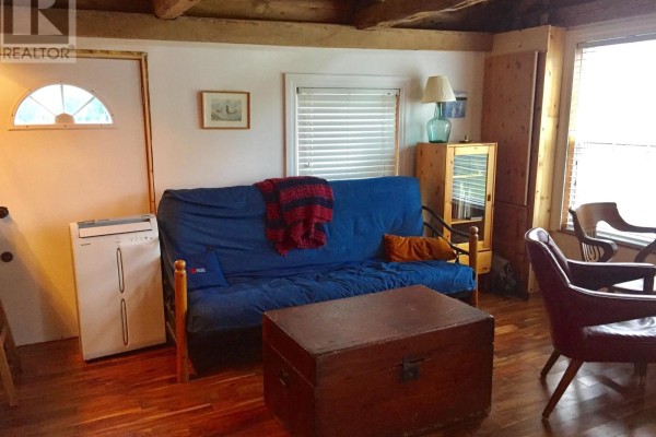 Living area with a blue futon, red blanket, wooden coffee table chest, and two chairs near a window. - 78 Marriotts Cove Road W, Marriotts Cove