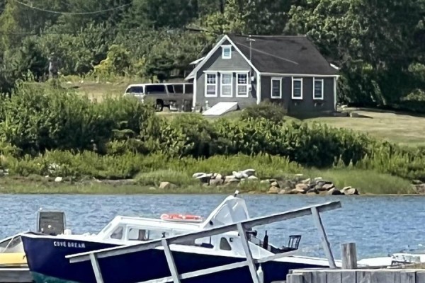 A grey cottage with white trim is visible behind lush green trees, with boats docked in the foreground water. - 78 Marriotts Cove Road W, Marriotts Cove
