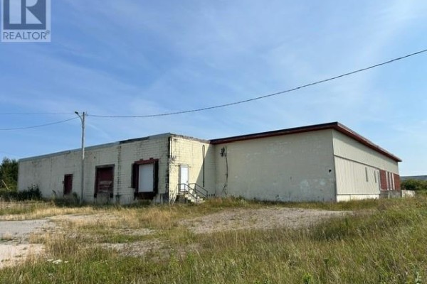 Side view of a beige commercial building with red accents, loading docks, and boarded windows. - 78 Missouri Drive, Stephenville