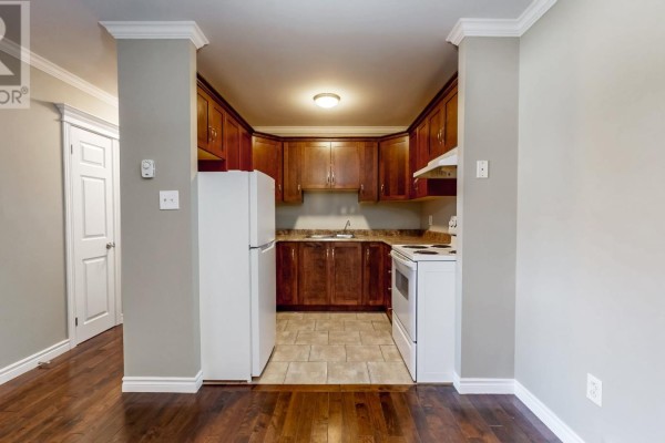 A compact U-shaped kitchen with dark wood cabinets, white appliances, and tiled flooring. - 78 Thorburn Road Unit#306, St John S