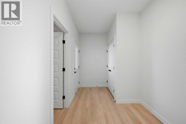 Interior hallway with light wood floors and white walls, leading to doors on the left and right. - 78 Waterford Mews, Chestermere