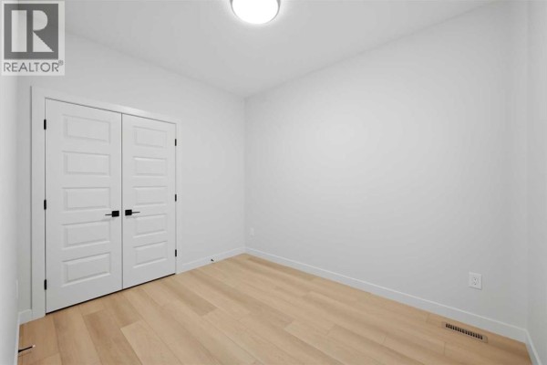 Empty room with light wood floors, white walls, and double white doors with black hardware. - 78 Waterford Mews, Chestermere