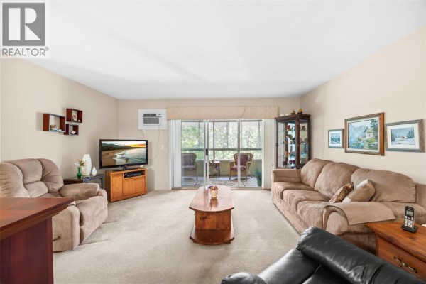 Living room with beige walls, carpet, sofa, chairs, coffee table, television, and balcony view. - 780 Houghton Road Unit# 408, Kelowna