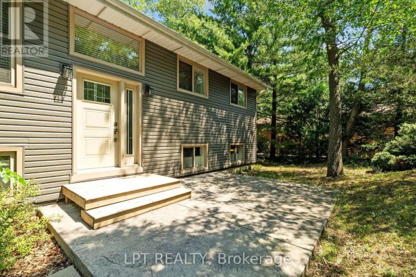 Aerial view of a house nestled among dense green trees, showing the roof and surrounding wooded area. - 7806 Alfred Crescent, Lambton Shores