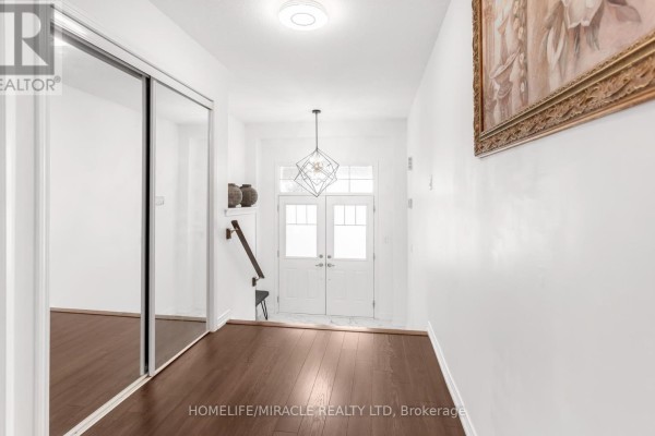 Interior view of a hallway with dark hardwood floors, mirrored closet doors, and a decorative chandelier. - 7808 Tupelo Crescent, Niagara Falls