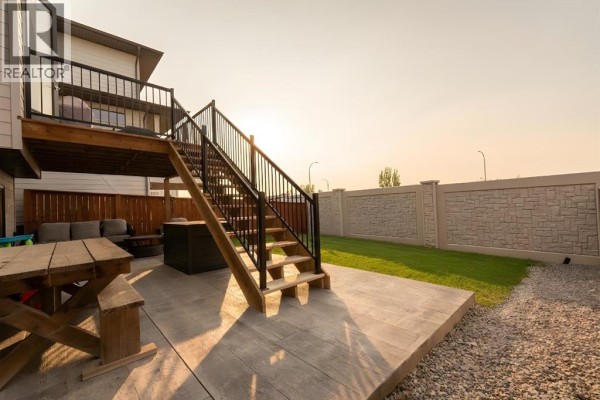 Panoramic view of houses on a street with a pond and undeveloped land in the background. - 781 Atlantic Cove W, Lethbridge