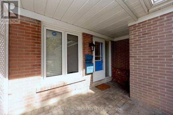 Covered front porch with brick walls, a white door, and windows, with stacked firewood to the side. - 781 Pam Crescent, Newmarket