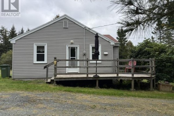 Side view of the house showing a wooden deck with a red chair and umbrella. - 7813 7 Highway, Musquodoboit Harbour
