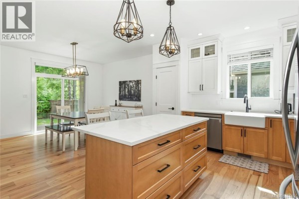 Open concept kitchen and dining area with island, light wood floors, and sliding glass door. - 782 Salal St, Campbell River