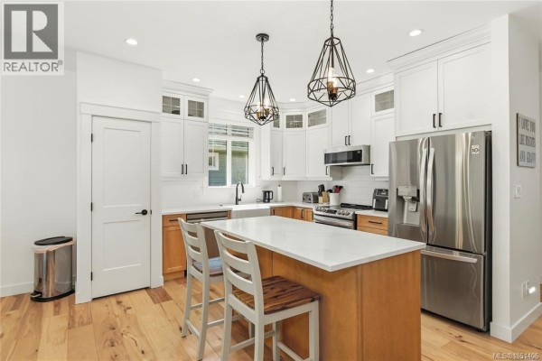 Modern kitchen with large island, white cabinets, stainless steel appliances, and farmhouse sink. - 782 Salal St, Campbell River