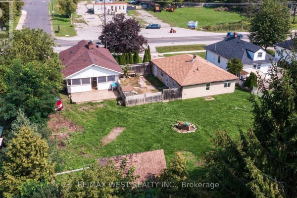 Rear view of two bungalows with wooden decks and fences, surrounded by green grass and trees. - 7826 Yonge Street, Innisfil