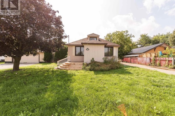 Front exterior of a small beige house with a gable roof and a green lawn. - 7826 Yonge Street, Innisfil