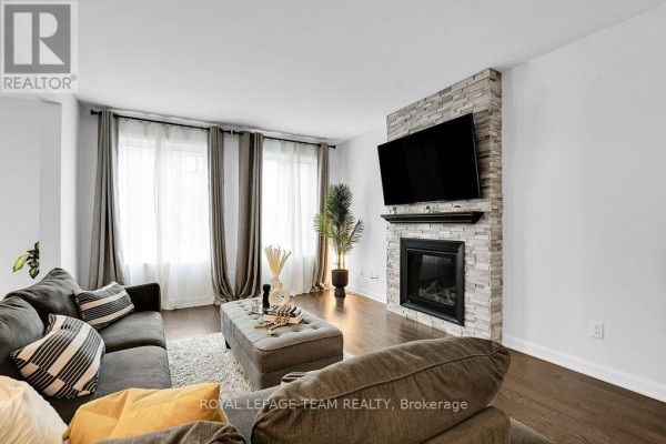 Living room with fireplace, mounted TV, sofa, ottoman, and large windows - 784 Cappamore Drive Ottawa