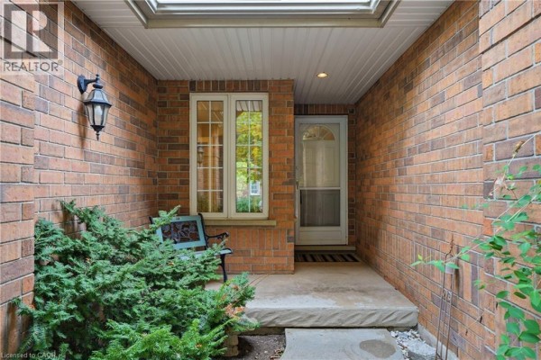 Covered front entryway with brick walls, glass door, and a small green bench. - 784 Gordon Street Unit# 20, Guelph
